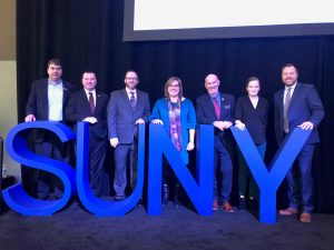 SUNYCUAD Board Members stand behind large blue SUNY letters.